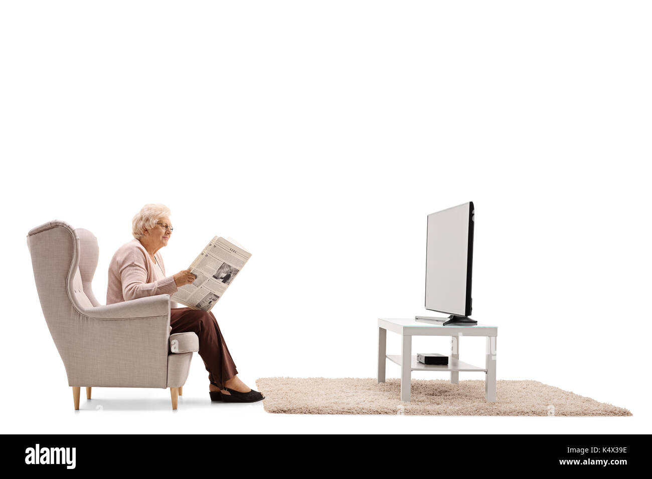 Femme âgée assise sur un fauteuil et la lecture d'un journal devant une télévision isolé sur fond blanc Banque D'Images