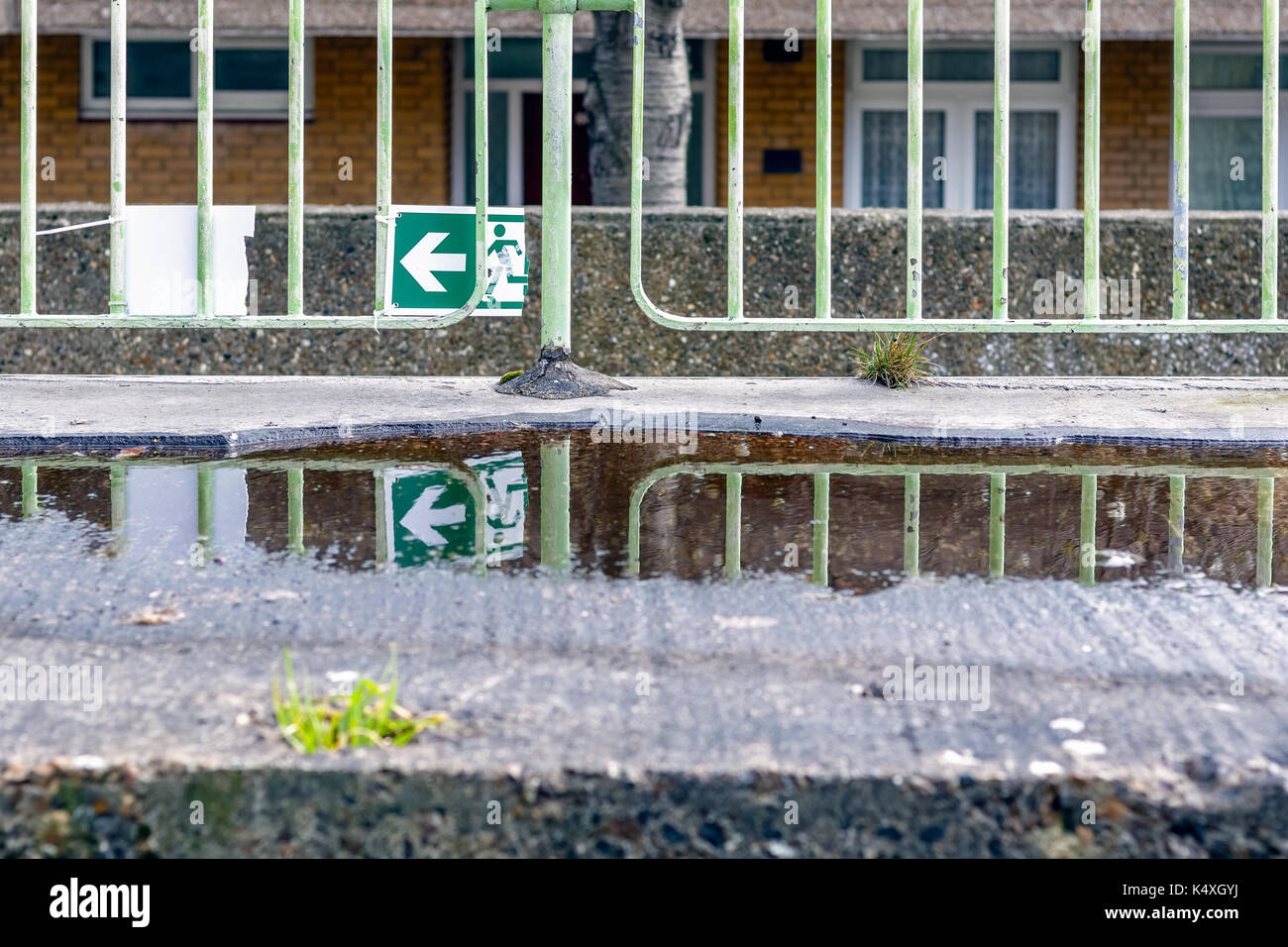Enseigne de sortie d'urgence vert cassé et son reflet dans une flaque d'eau pour l'utilisation du concept Banque D'Images