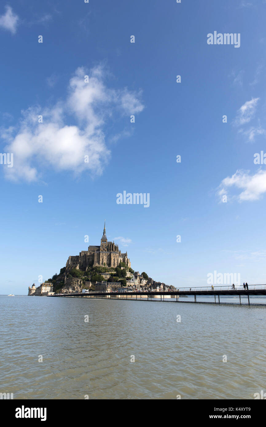 Le Mont-Saint-Michel et l'abbaye entourée d'eau et les touristes la marche sur la passerelle. Ciel bleu Banque D'Images