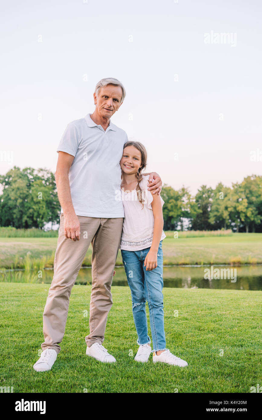 Smiling grandfather and granddaughter hugging chaque autres et looking at camera on meadow Banque D'Images