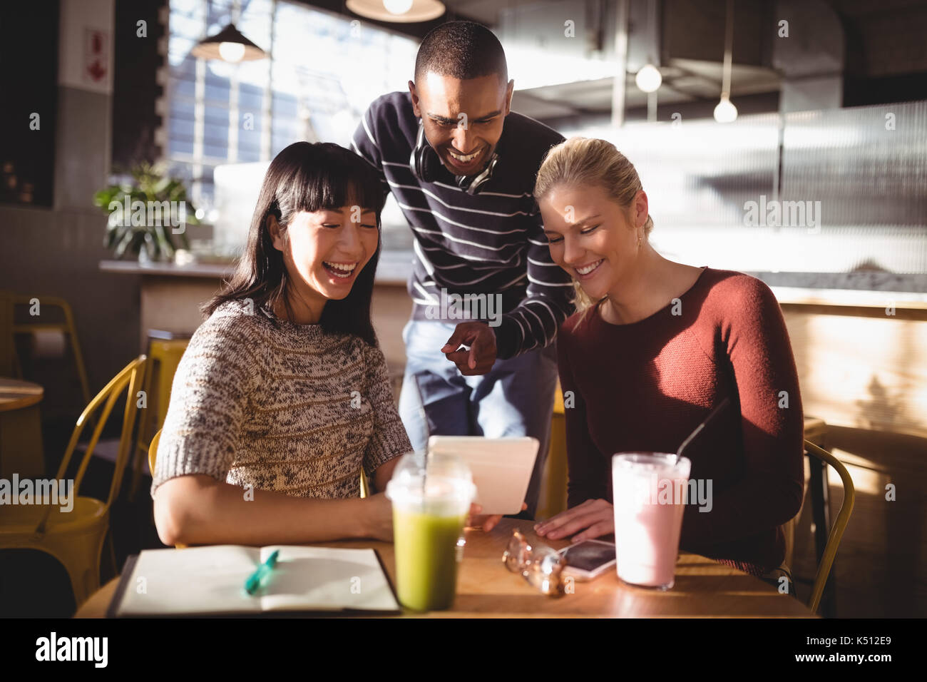 Smiling man pointing at digital tablet en se tenant debout au milieu d'amies in coffee shop Banque D'Images