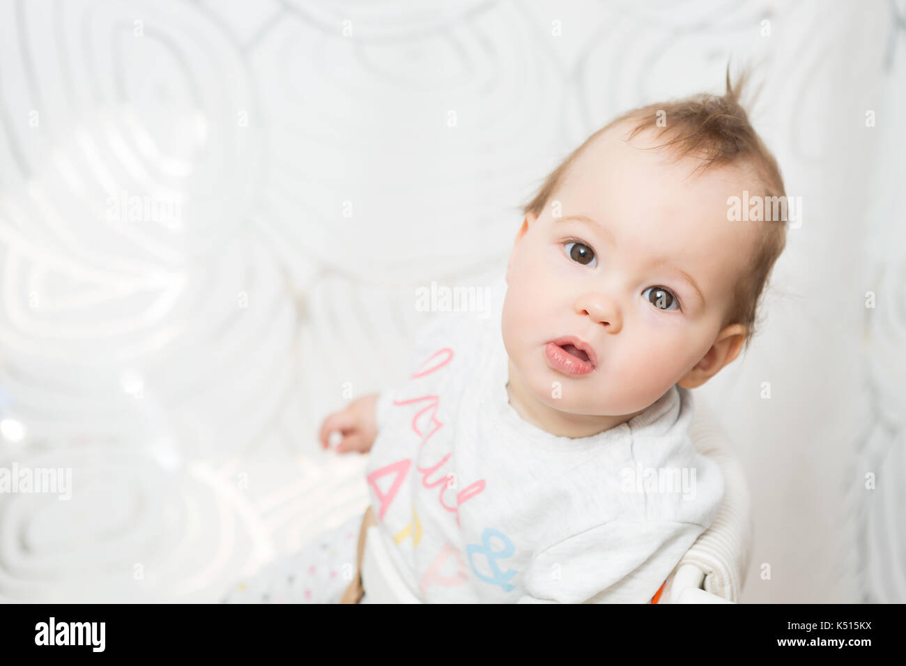 Onze mois baby girl sitting dans un tabouret pour faire des grimaces dans l'appareil photo, vue d'en haut Banque D'Images