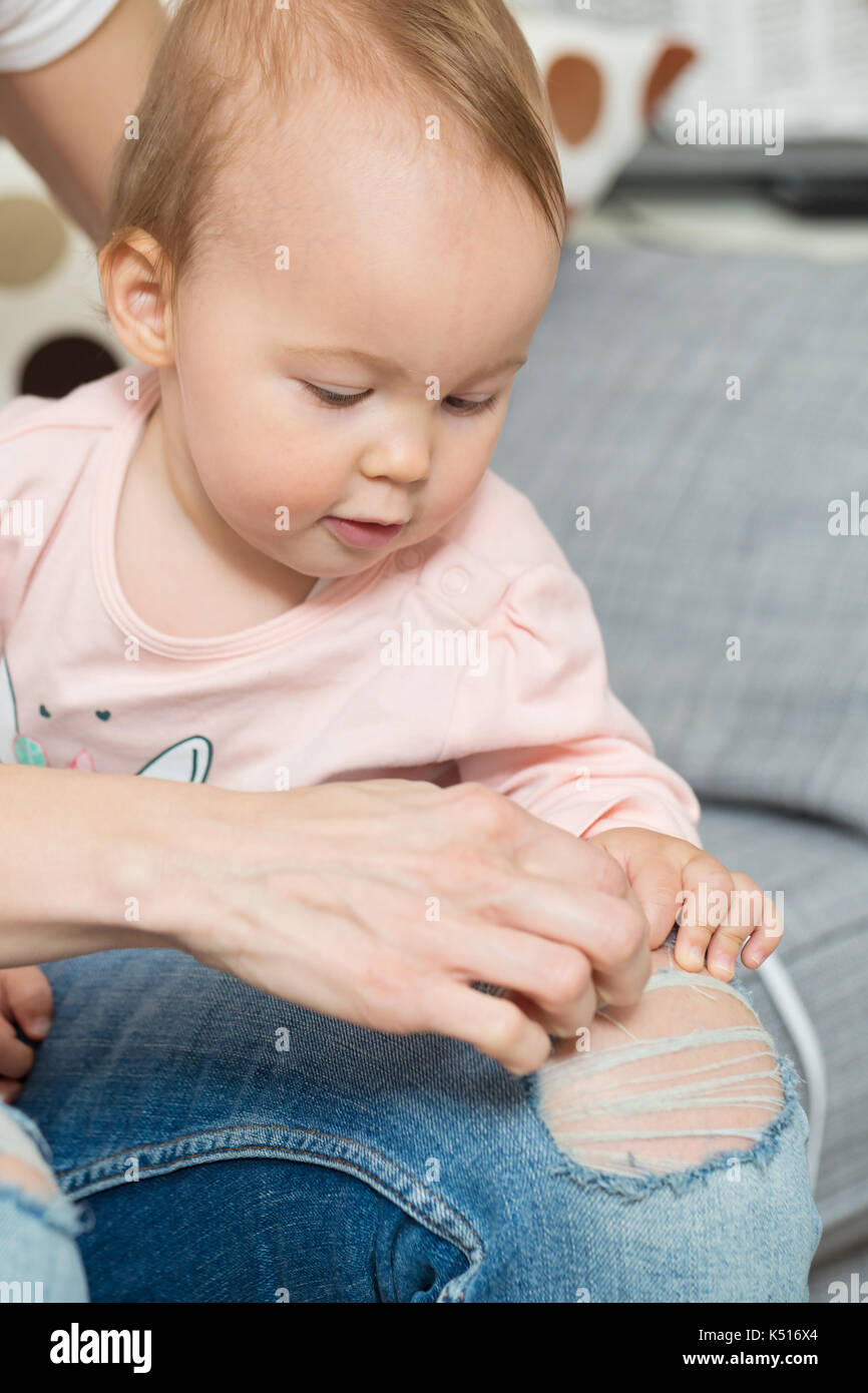 Un an bébé fille jouant avec sa mère, pantalon denim déchiré Banque D'Images