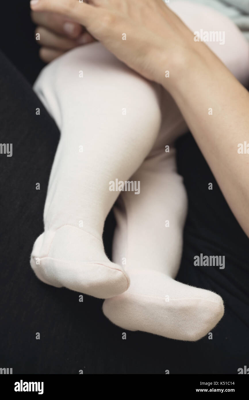 Les jambes du bébé habillé en petit bas sur les genoux de sa mère pendant l'allaitement, mother's hand holding le bébé nouveau-né Banque D'Images