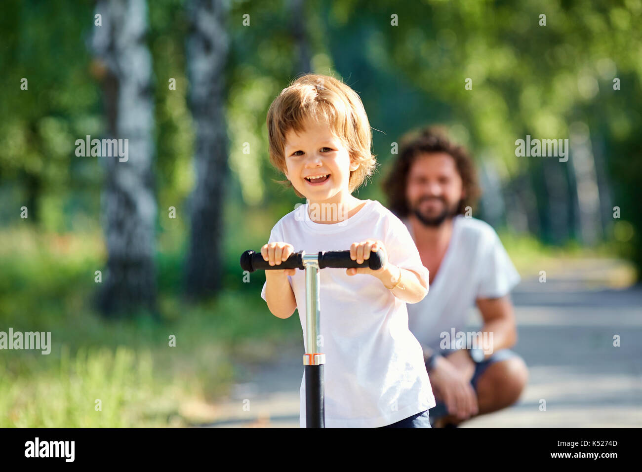 Le garçon patins sur un scooter dans le parc avec son père Banque D'Images