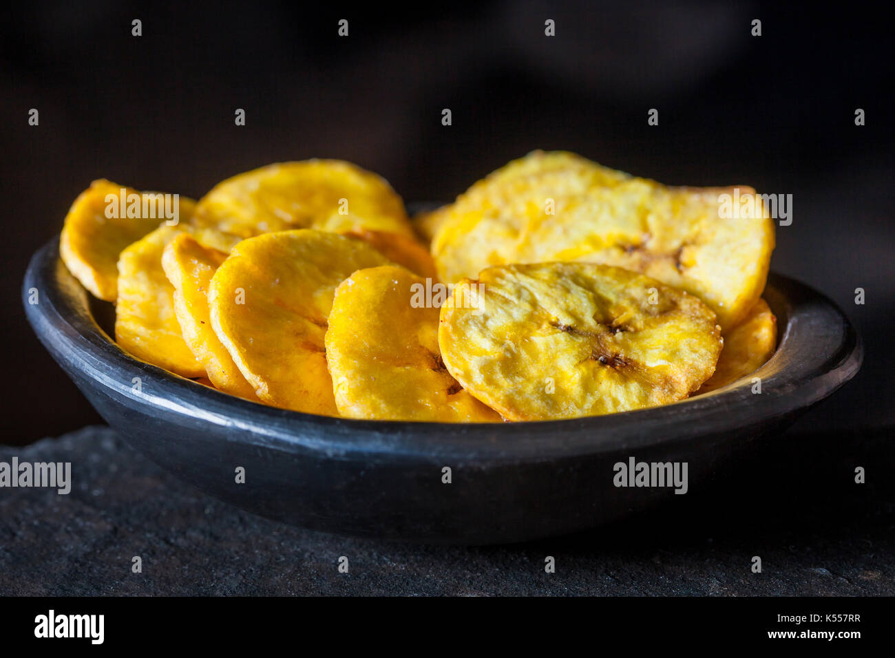 Le plantain poêlée de pièces dans une cuvette d'argile noir sur fond noir Banque D'Images