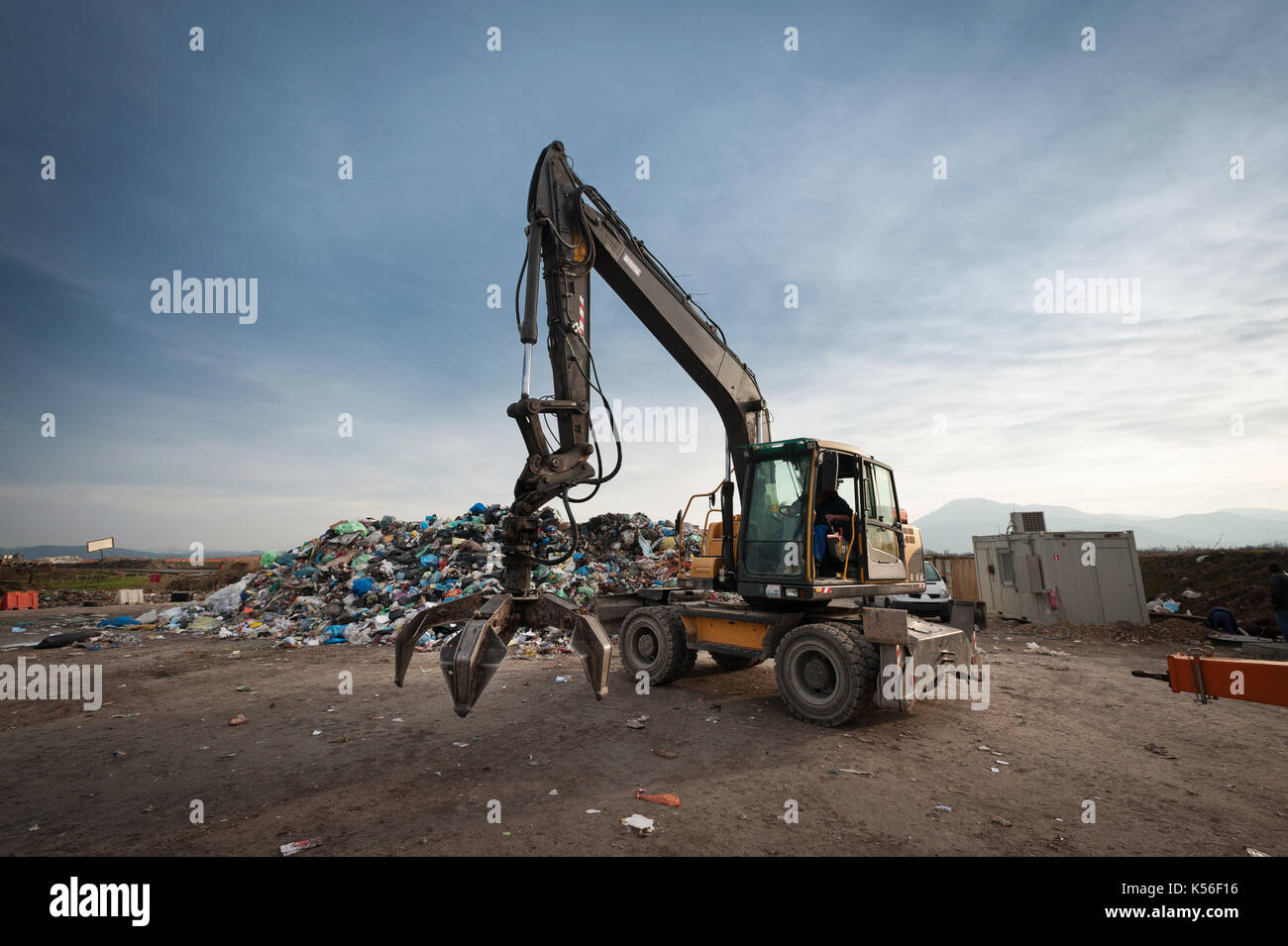 Bulldozer avec bras mécanique saisissant d'un tas de déchets à l'enfouissement de la ville. La gestion des déchets, de l'écologie concept. Banque D'Images