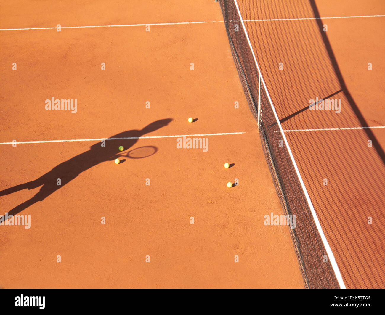 Ombre de joueur de tennis à net avec scatttered les balles de tennis sur terre battue Banque D'Images
