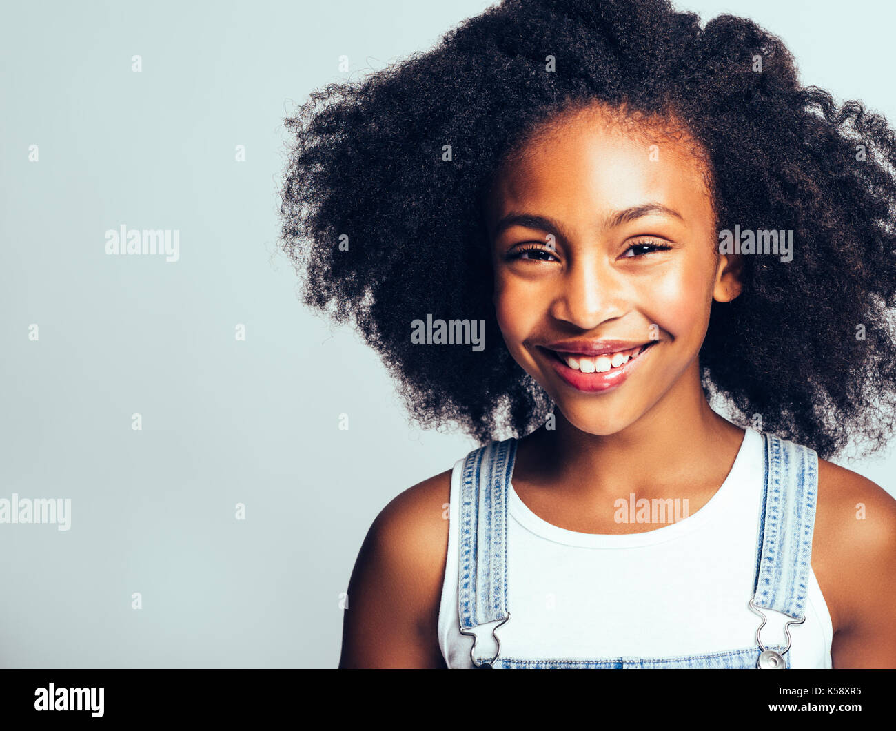 Jeune Fille Africaine Avec De Longs Cheveux Boucles De Sourire Et De Porter Bebe En Position Debout Par Elle Meme Sur Un Arriere Plan Gris Photo Stock Alamy