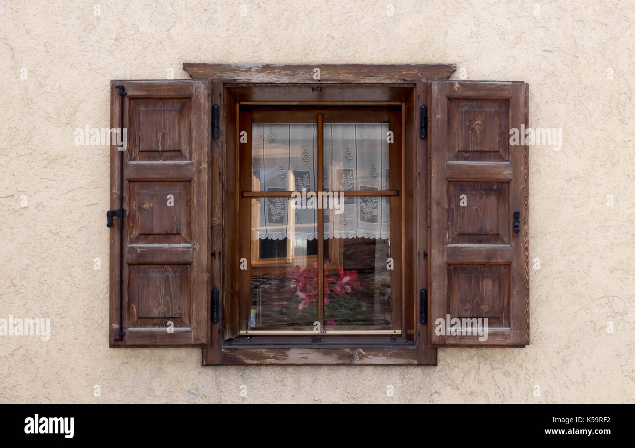 Vieille fenêtre en bois avec volets en bois naturel ouverte dans un mur de plâtre rugueux à la crème avec des reflets sur les vitres Banque D'Images