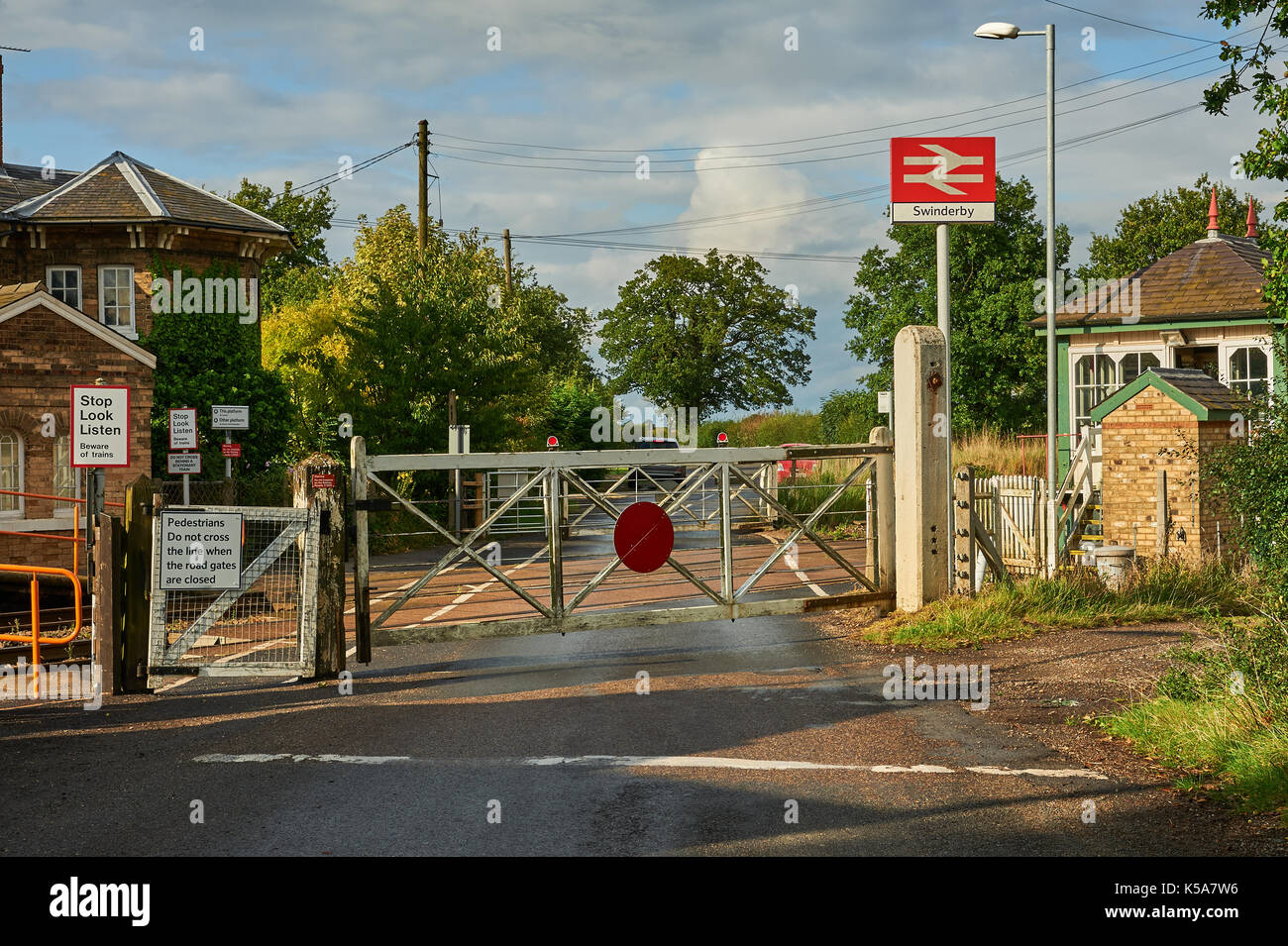 Les trains et les barrières du passage à niveau à commande manuelle dans le petit village de Rungis Lincolnshire Banque D'Images