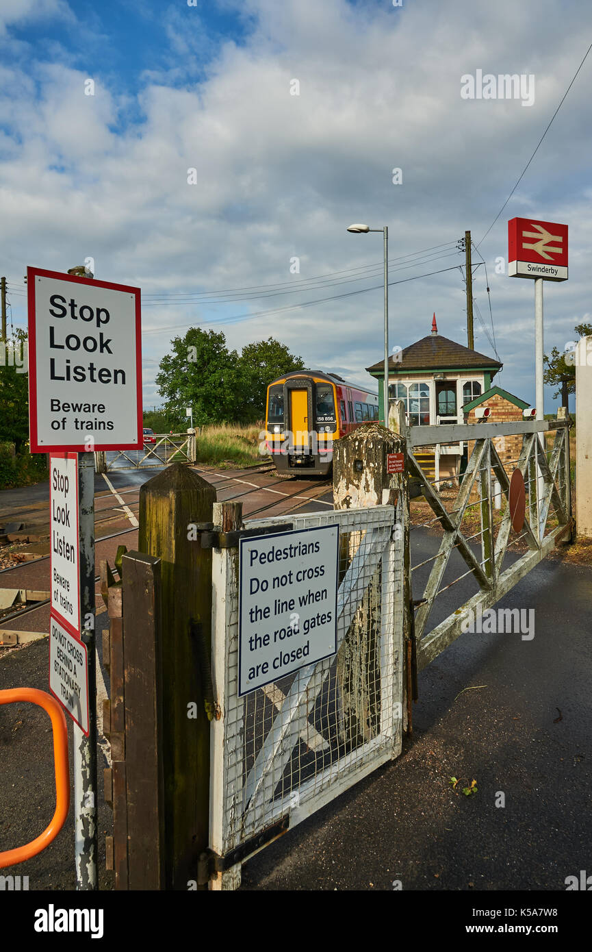 Les trains et les barrières du passage à niveau à commande manuelle dans le petit village de Rungis Lincolnshire Banque D'Images