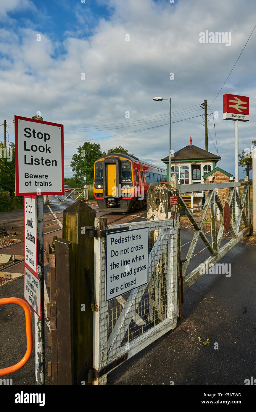 Les trains et les barrières du passage à niveau à commande manuelle dans le petit village de Rungis Lincolnshire Banque D'Images