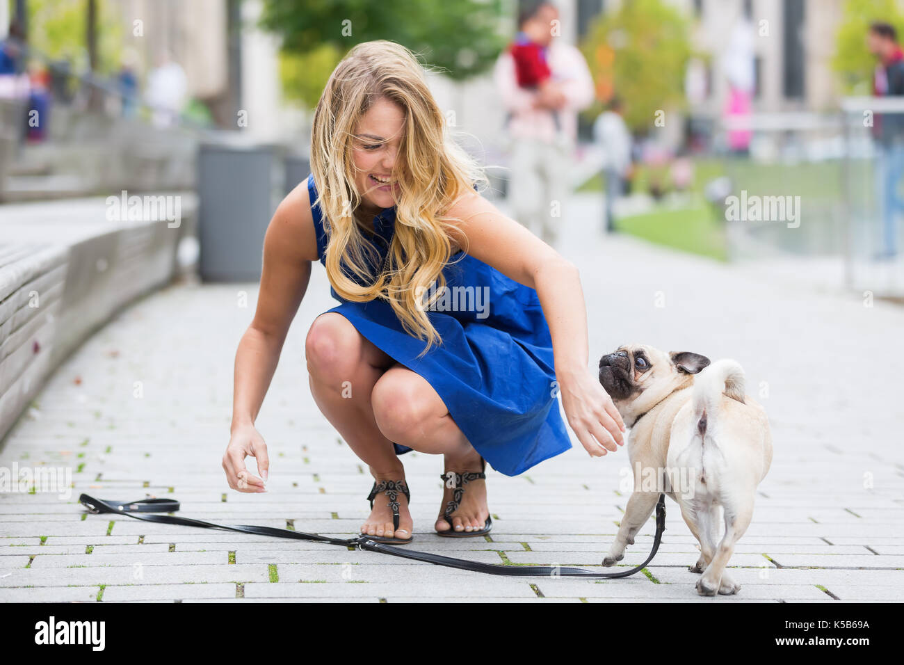 Jolie jeune femme joue avec un adorable carlin sur une route Banque D'Images