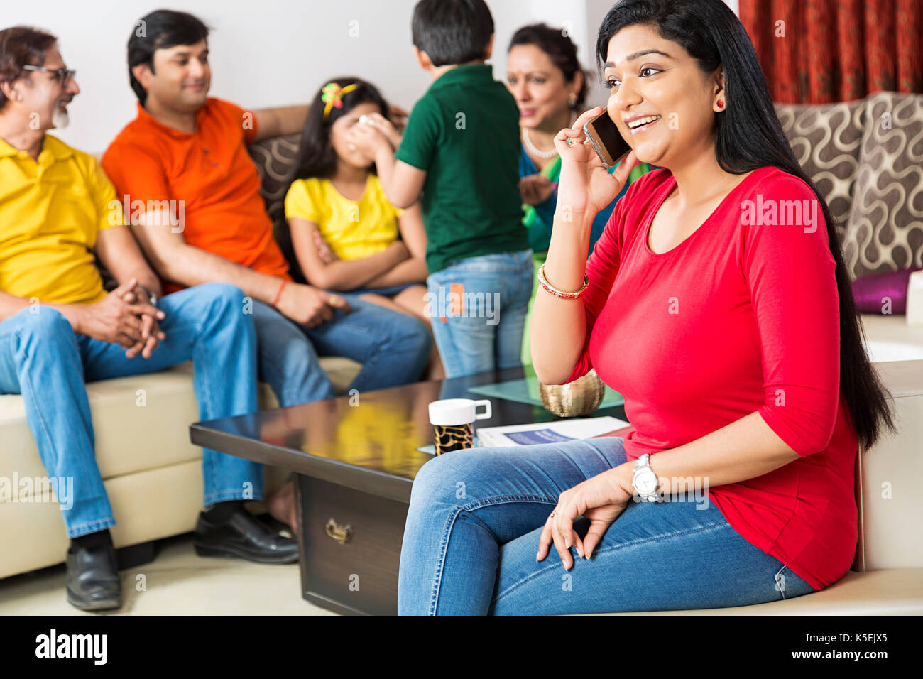 Family sitting canapé avec leur femme qui parle en premier plan de téléphone à la maison Banque D'Images