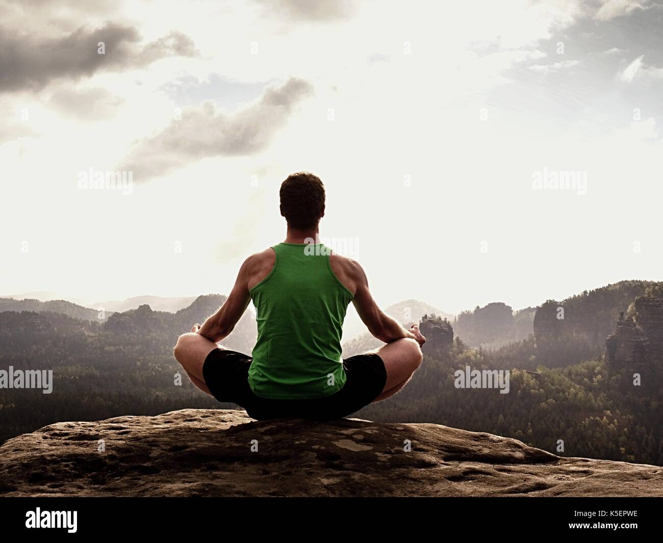 Seul l'homme est le yoga font peser sur les rochers à l'intérieur de pointe matin brumeux. homme d'âge moyen pratique le yoga et la méditation dans les montagnes pendant la météo de luxe Banque D'Images