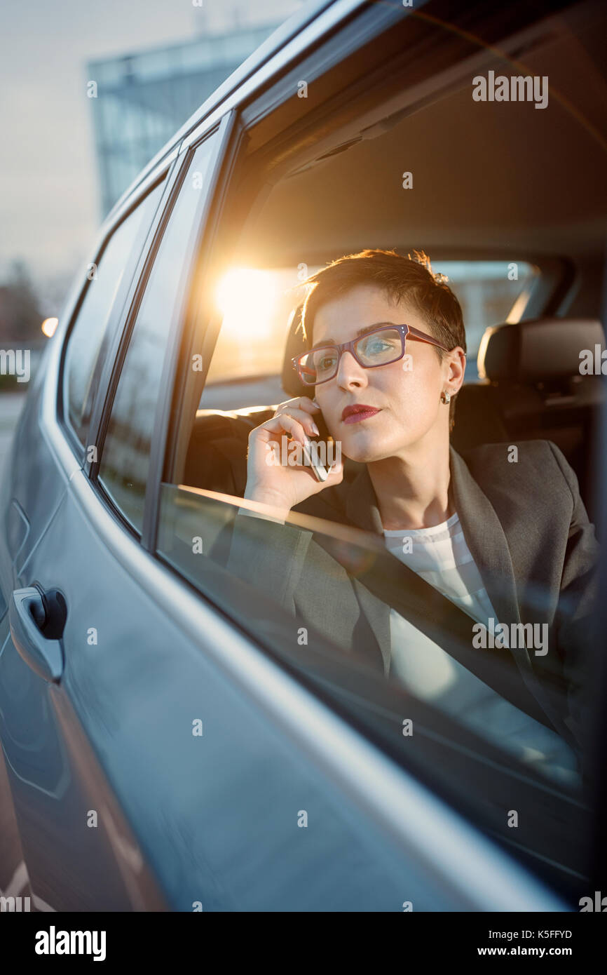 Jeune femme d'affaires est la conduite dans une voiture et l'utilisation smartphone Blackberry Banque D'Images