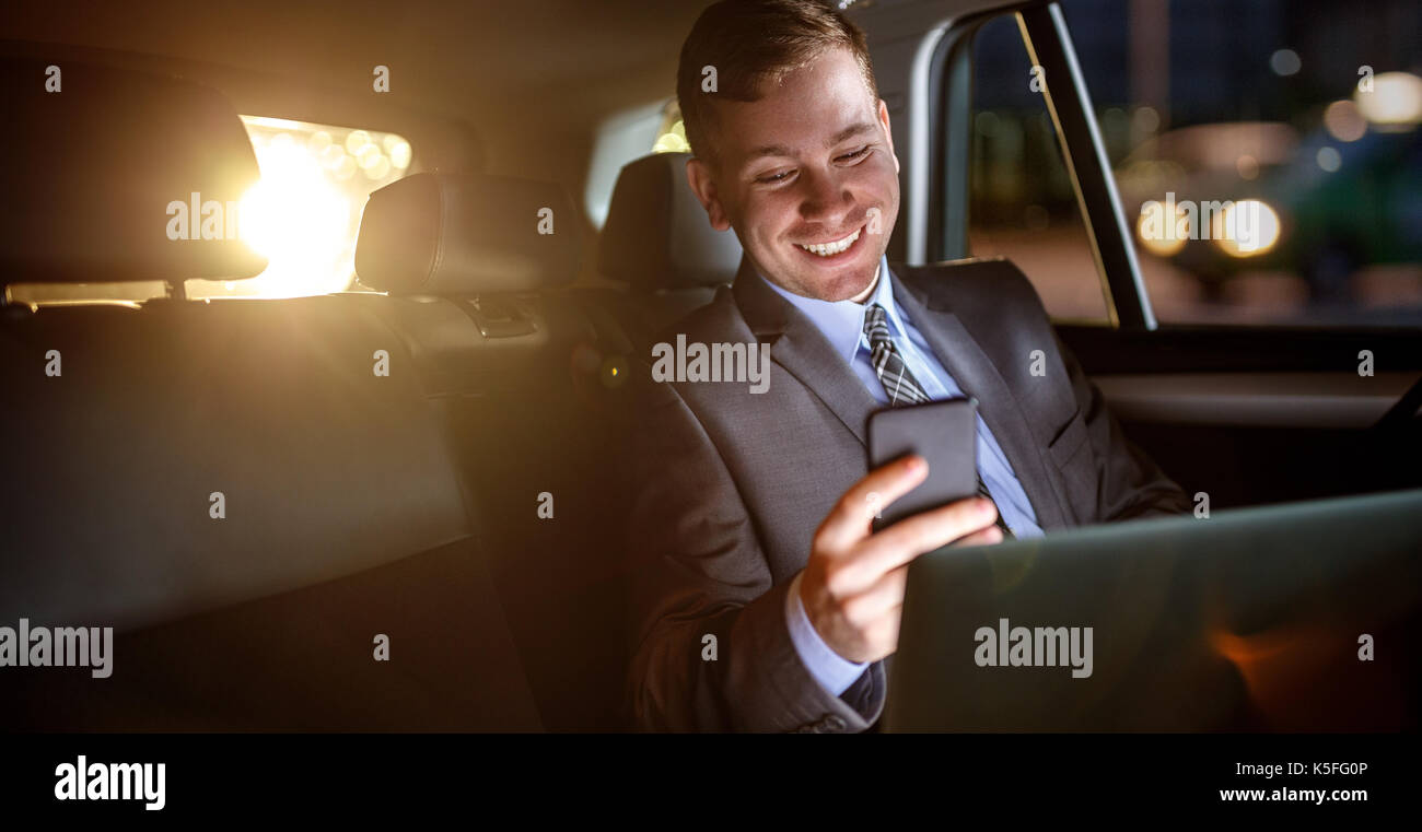 Smiling businessman travailler sur late night in back seat of car Banque D'Images