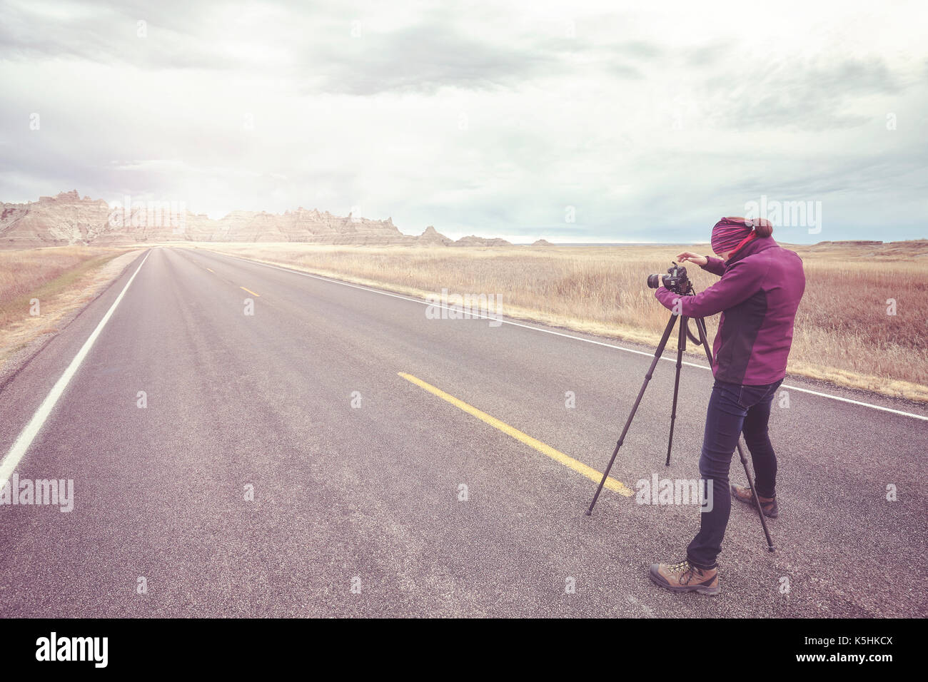Photographe de paysage prend des photos sur une route vide au coucher du soleil, harmonisation des couleurs appliquées, voyager ou travailler concept, Badlands National Park (Dakota du Sud), Banque D'Images