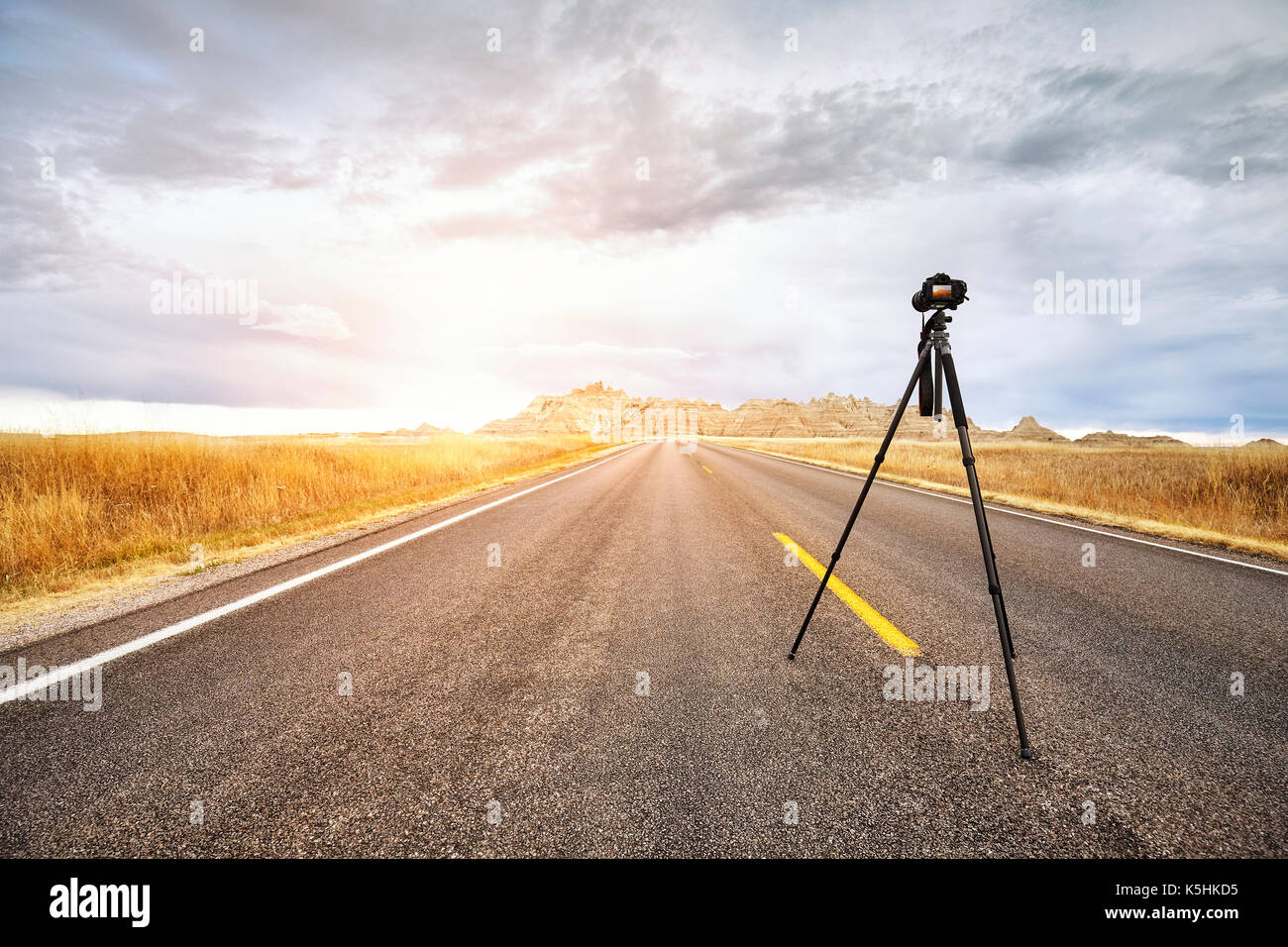 Appareil photo sur trépied photo professionnel sur une route vide au coucher du soleil, l'accent sur l'appareil photo de voyage ou de travail, concept, Badlands National Park, South Dakota, USA Banque D'Images