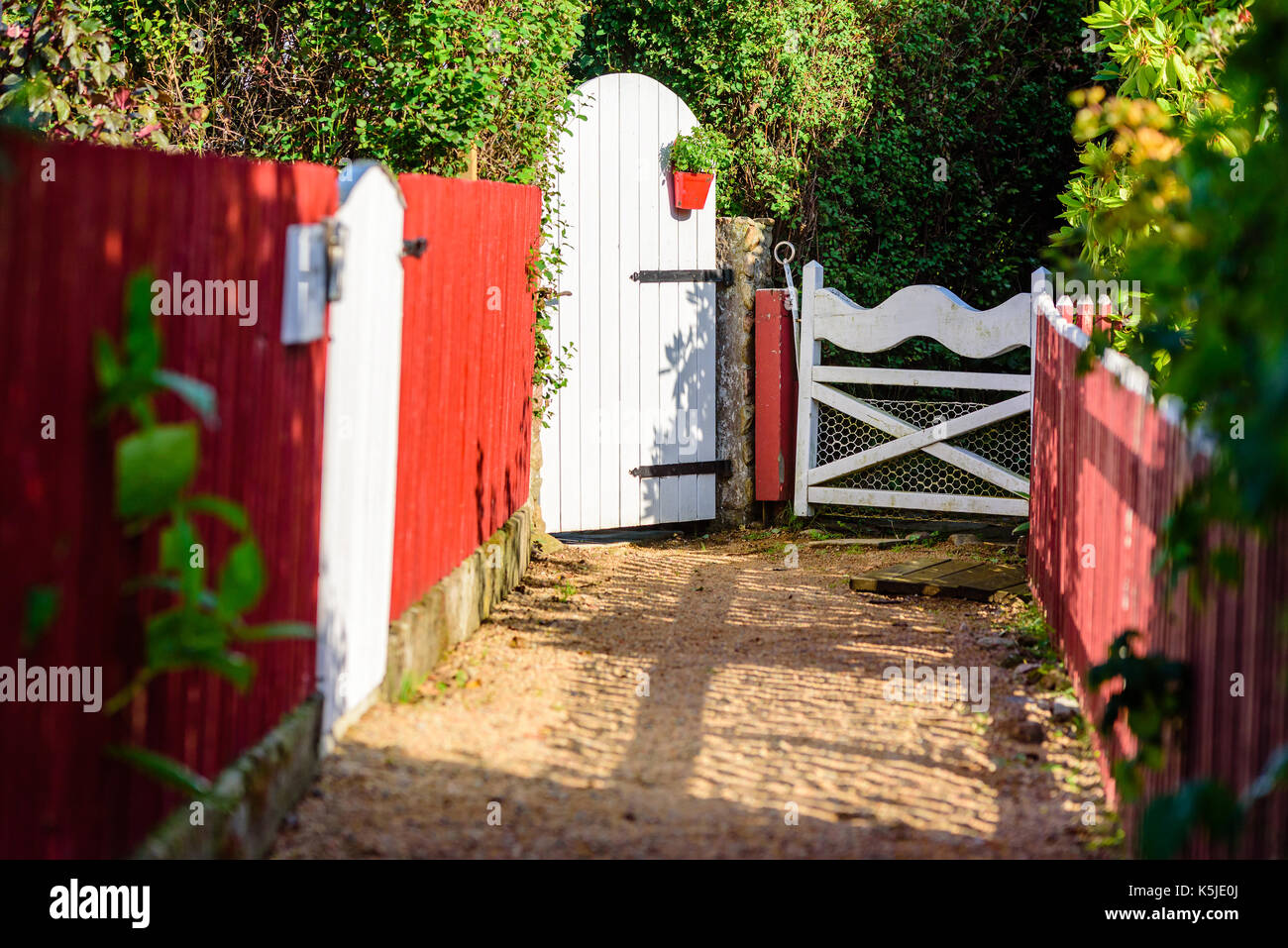 White garden gates à la fin d'un sentier de gravier. Rouge clôture côtés la lane. cache-pot en fin d'embarquement. Banque D'Images