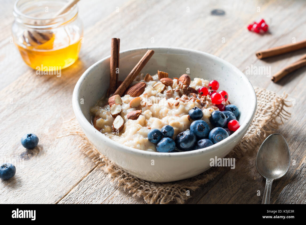 Gruau d'avoine avec des bleuets, amandes, cannelle, miel, linseeds et groseilles rouges dans un bol. super aliment pour petit-déjeuner nutritif sain Banque D'Images