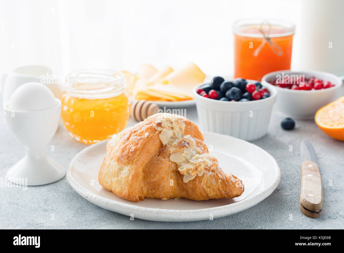 Croissant aux amandes, miel, de bleuets frais, orange, confiture, groseilles, oeuf mollet et bouteille de lait sur la table . vue rapprochée d'un petit-déjeuner continental. cop Banque D'Images