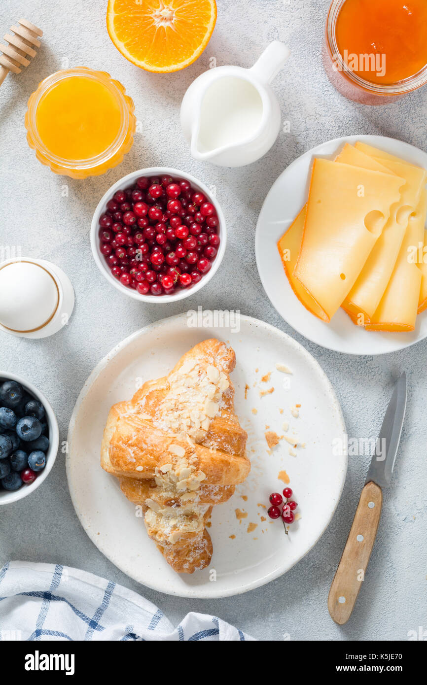 Le petit déjeuner continental en vue de dessus de table. des croissants frais, œuf dur, fromage, confiture, miel, orange, crème, les bleuets et les raisins sur table bleu vif. Banque D'Images