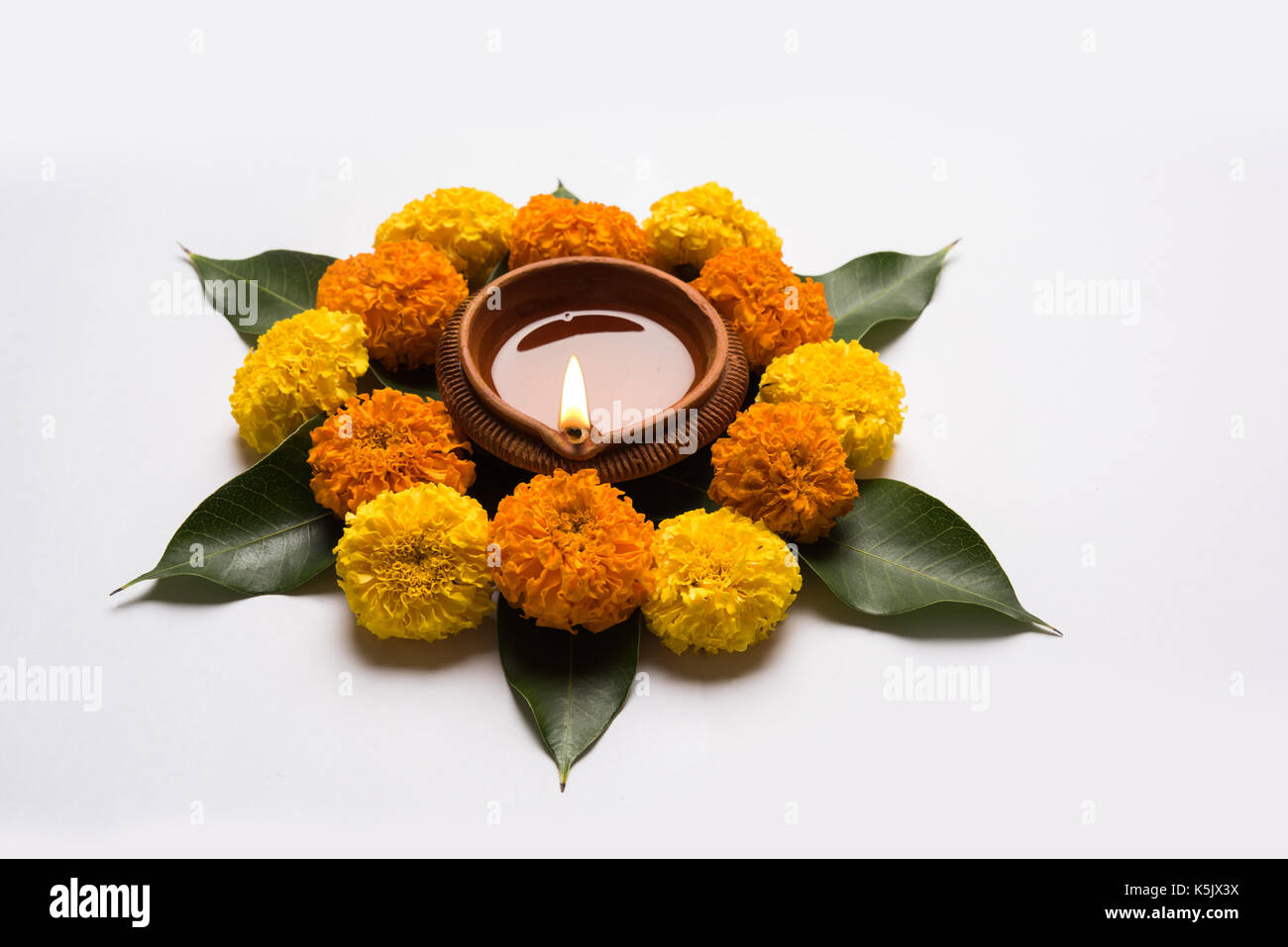 Rangoli fleur pour diwali ou pongal ou faite à l'aide de l'œillet d'Onam ou zendu fleurs et pétales de rose rouge sur fond blanc avec diwali diya au milieu Banque D'Images