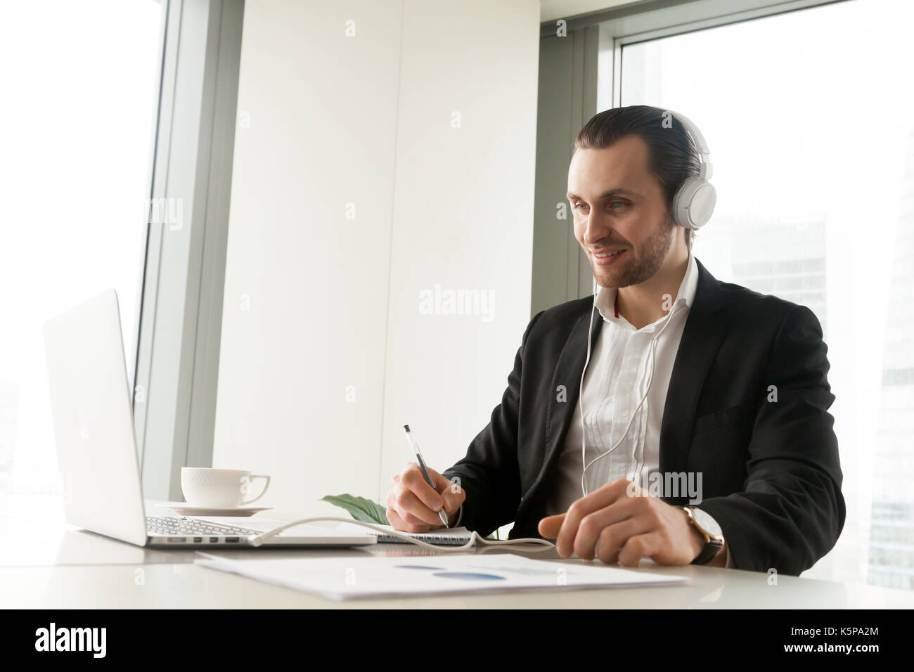 Businessman in headphones prise de notes en face de l'ordinateur portable. Banque D'Images