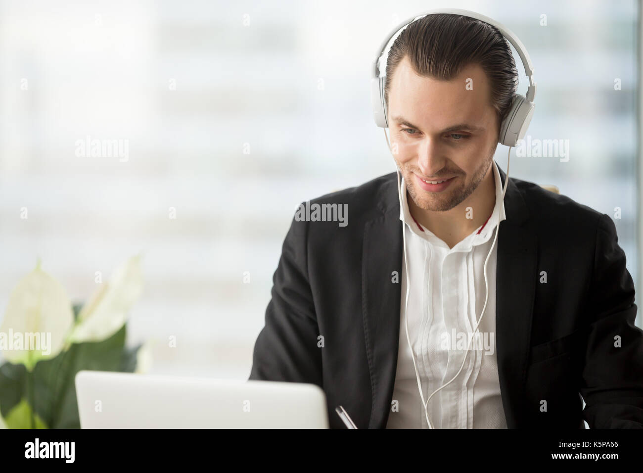 Smiling businessman dans les écouteurs à la recherche à l'écran du portable. Banque D'Images
