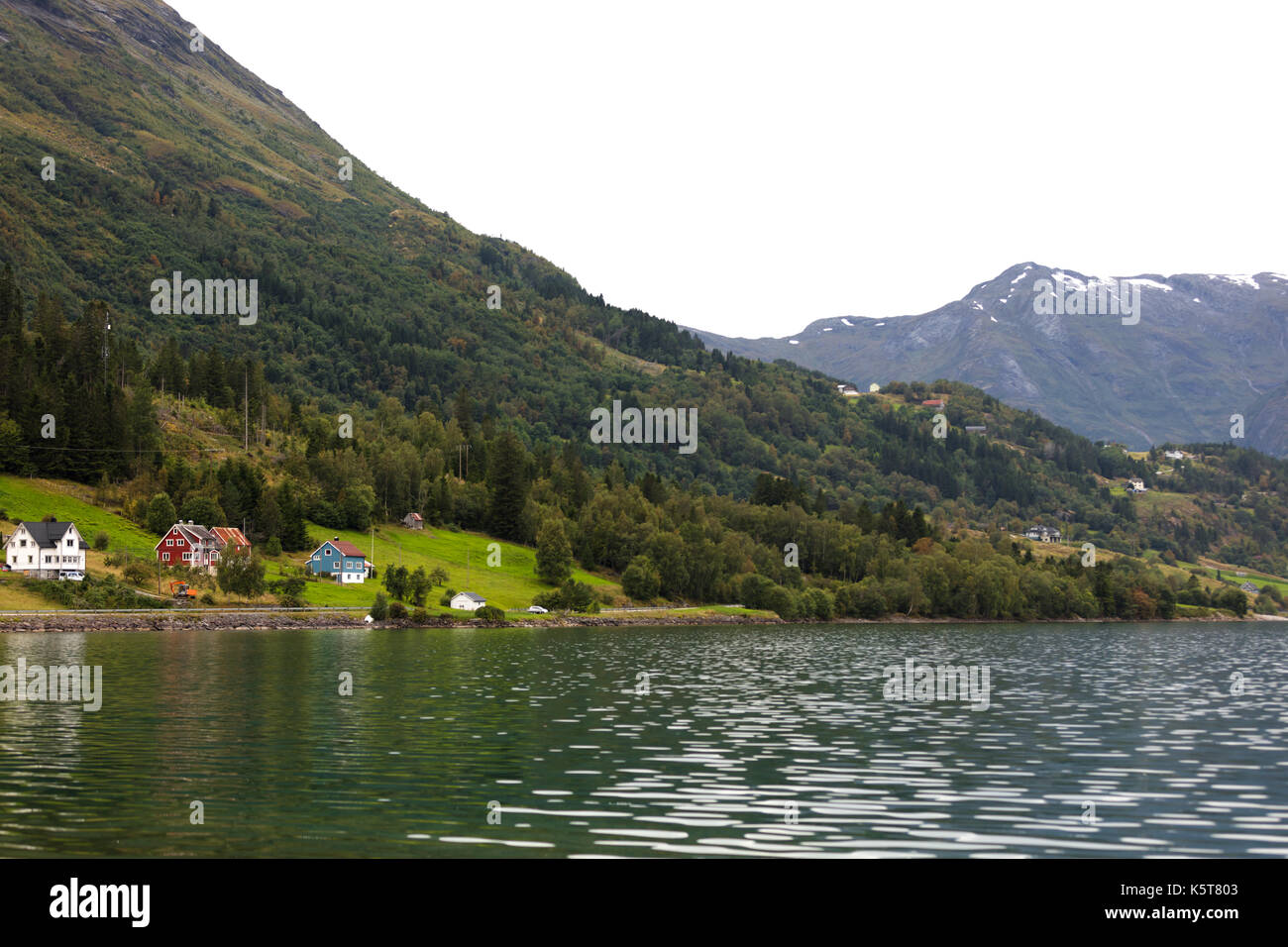 Paysage norvégien au pied d'un lac avec des forêts et montagnes enneigées en arrière-plan Banque D'Images