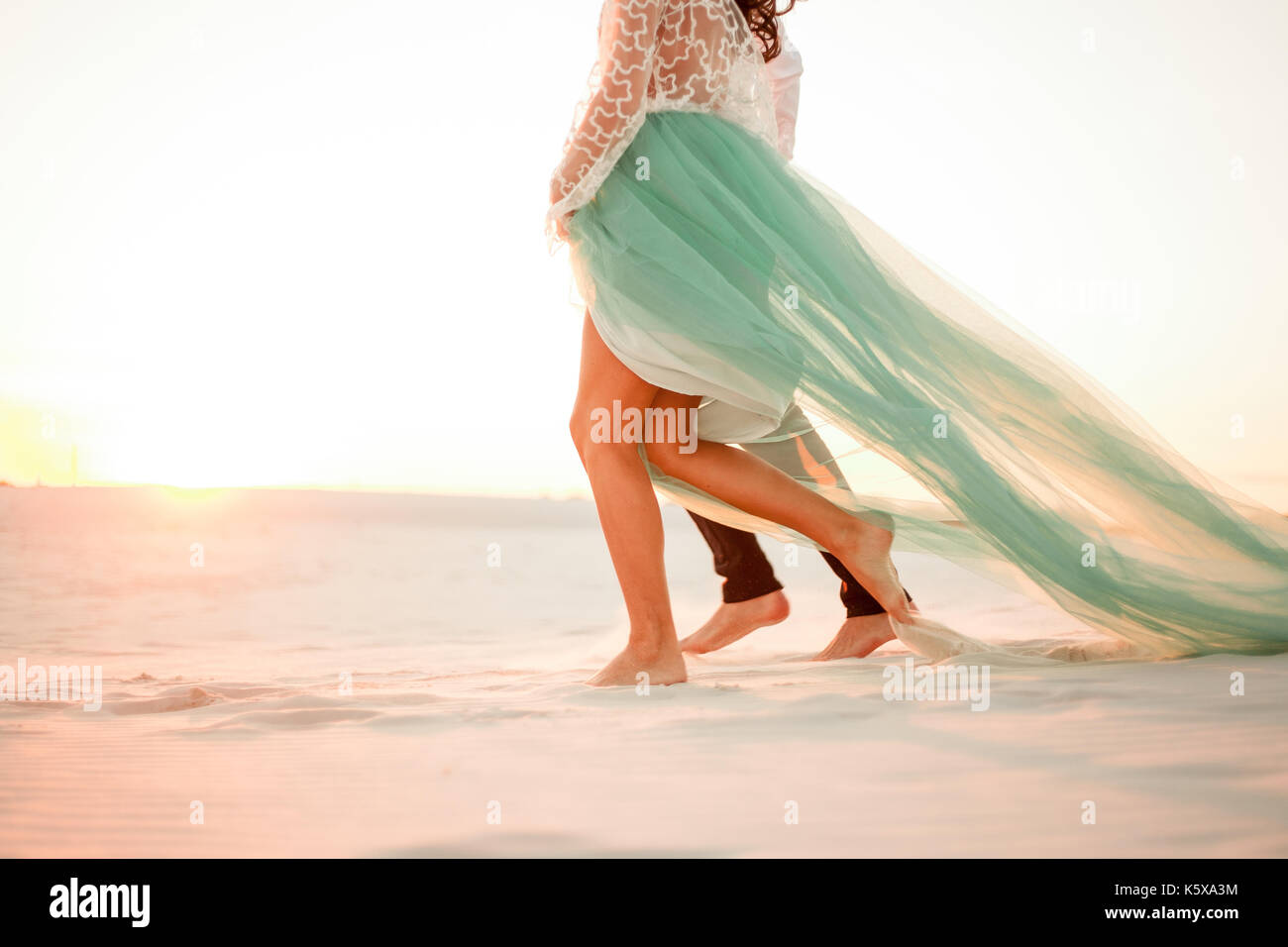Les jambes de la jeune mariée et se toilettent marche pieds nus sur du sable dans le désert au coucher du soleil. close up. Banque D'Images