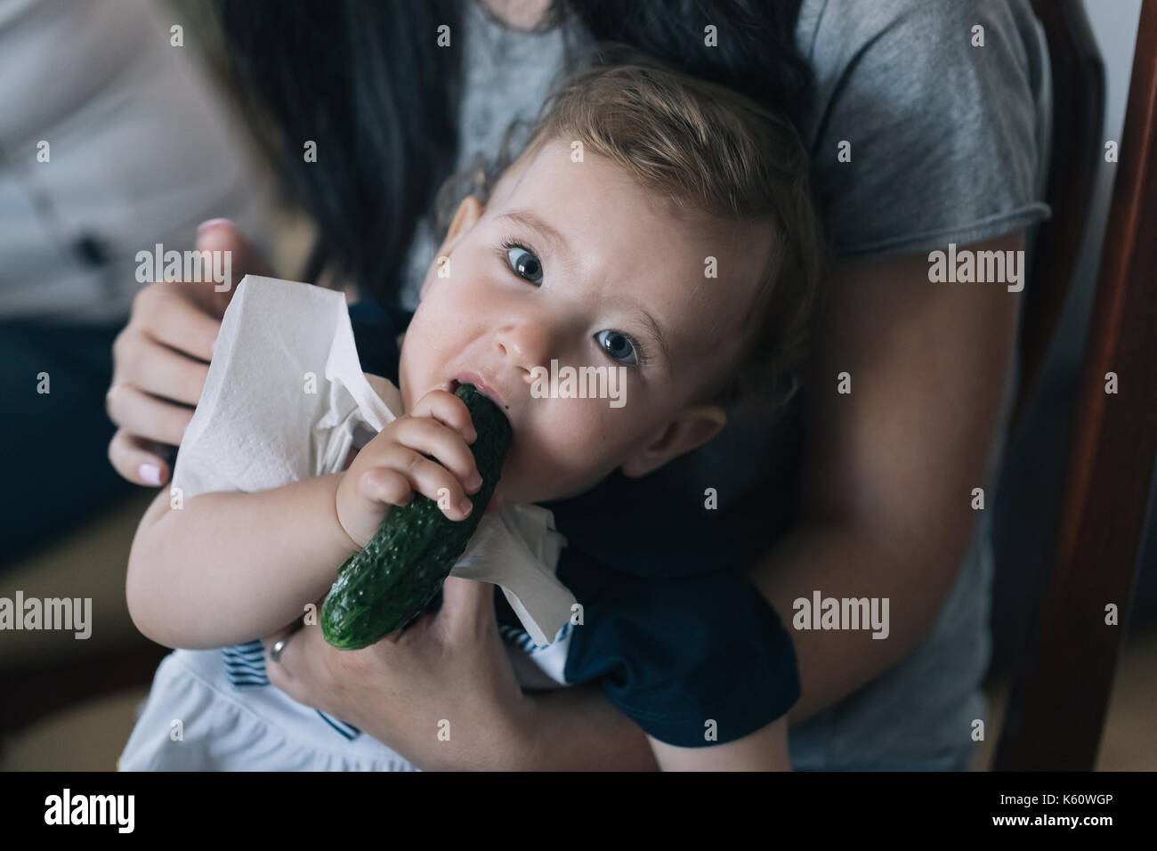 Petit bébé dans les bras d'une mère ronge un concombre. Banque D'Images