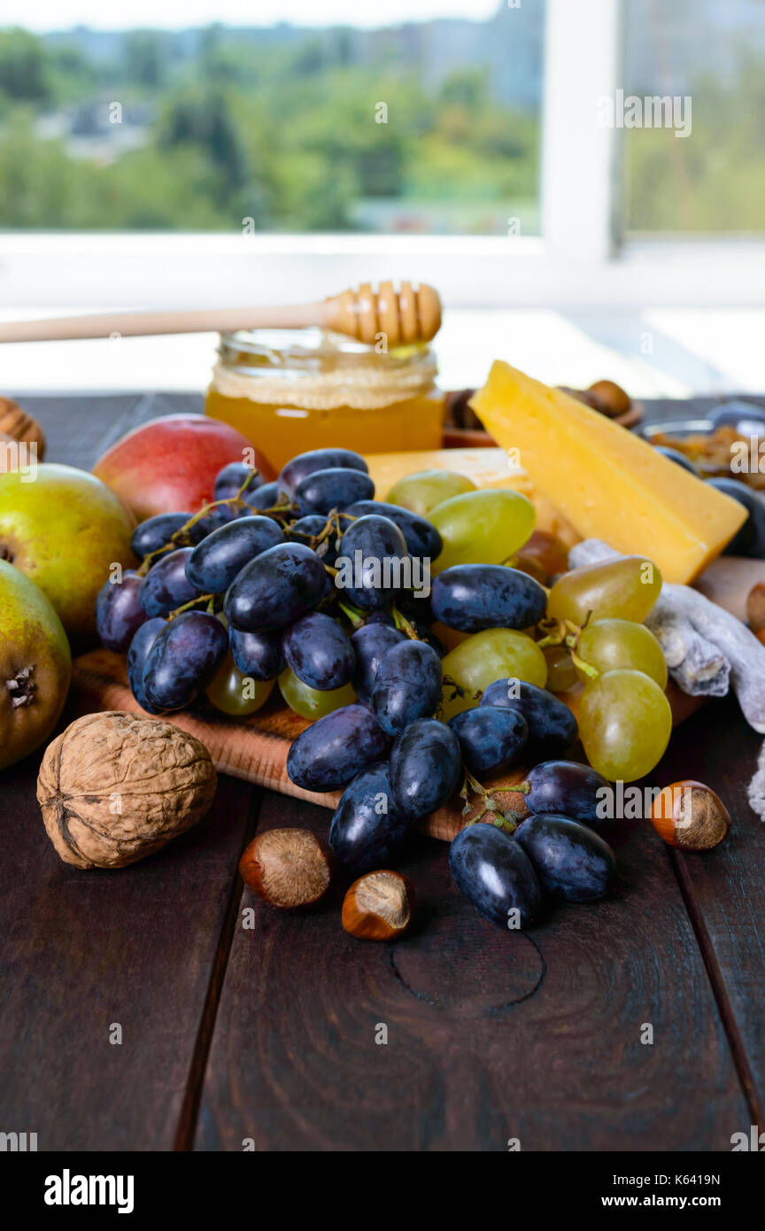 Un ensemble de produits : raisins, noix, miel, poires, fromage sur une table en bois foncé près de la fenêtre. Banque D'Images