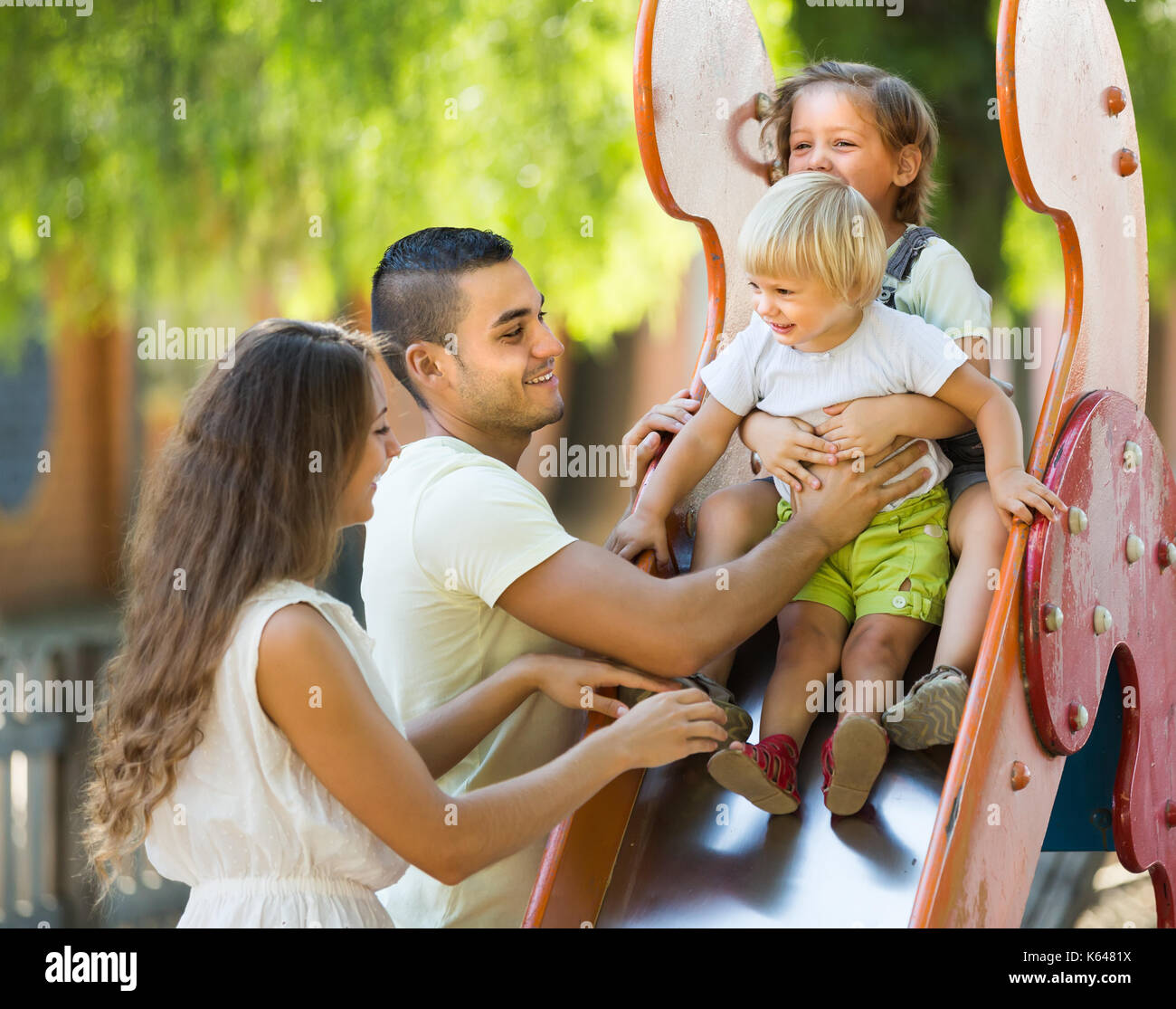 Famille heureuse positive de quatre au parc de jeux pour enfants, en Banque D'Images