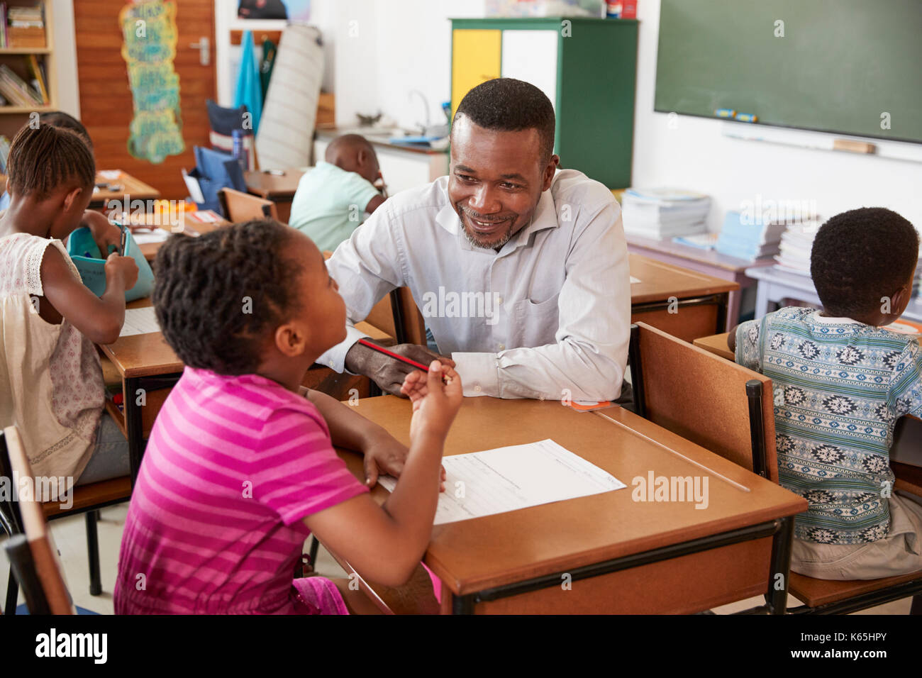 Mâle noir aider l'enseignant dans la classe fille de l'école élémentaire Banque D'Images