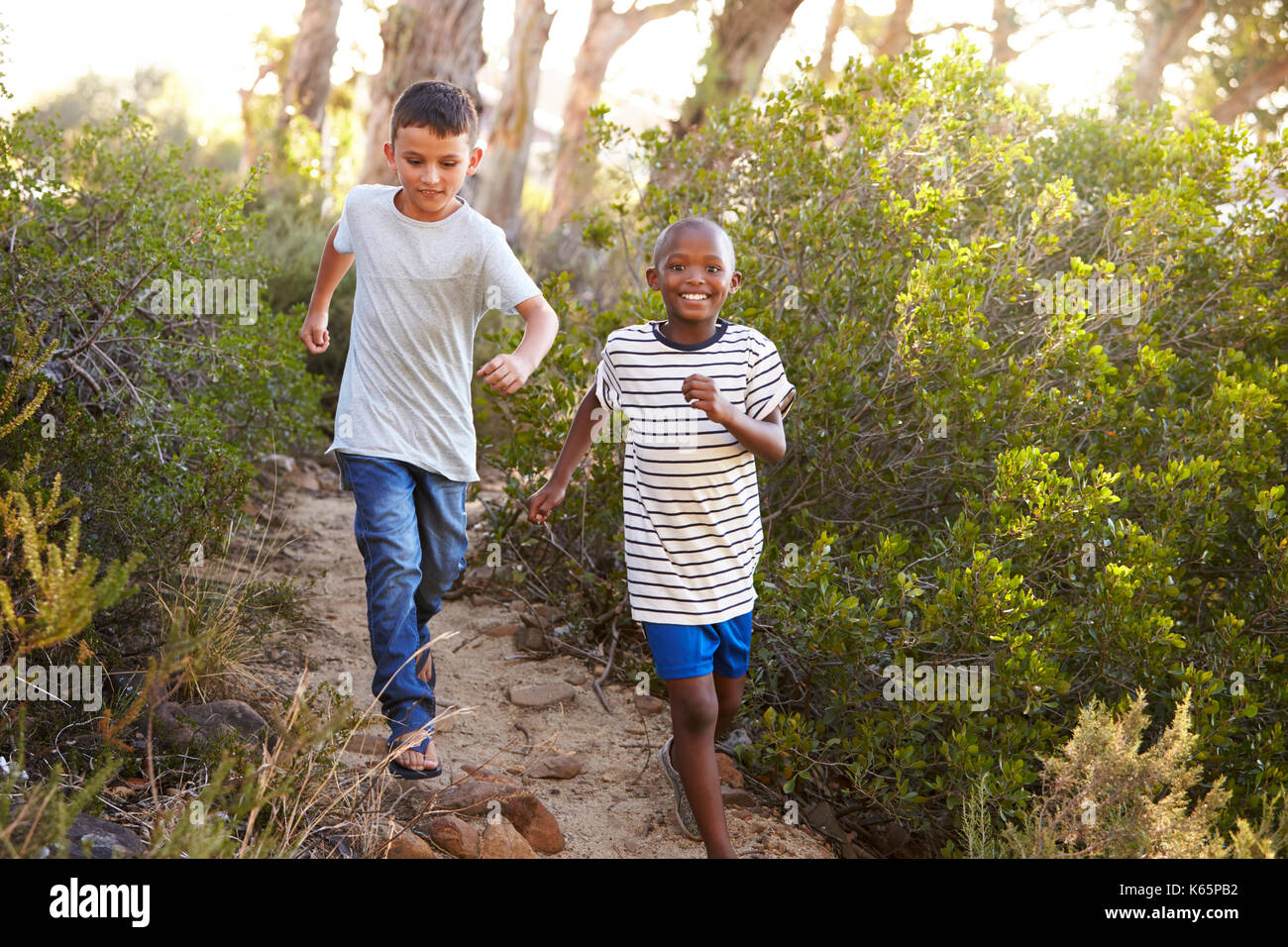 Deux jeunes garçons souriants racing sur un chemin forestier Banque D'Images