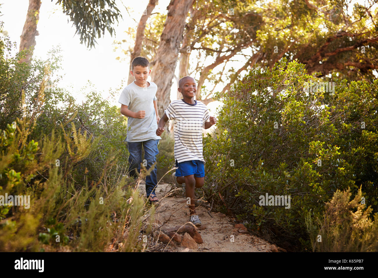 Deux jeunes garçons souriants courant le long d'un chemin forestier Banque D'Images