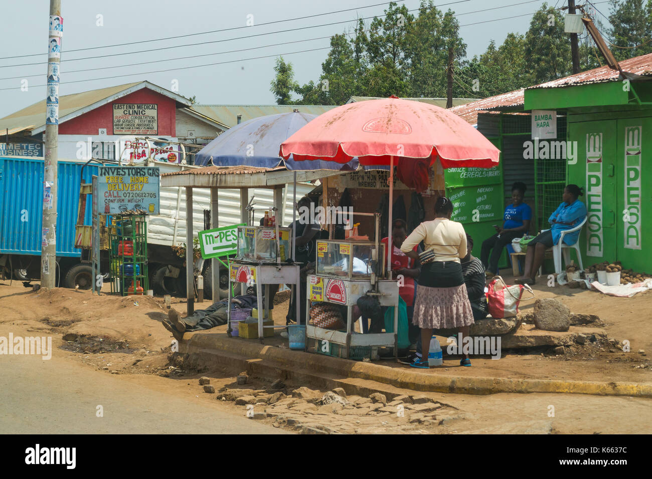 Les femmes s'asseoir à l'ombre des parasols food par route en ville, au Kenya Banque D'Images