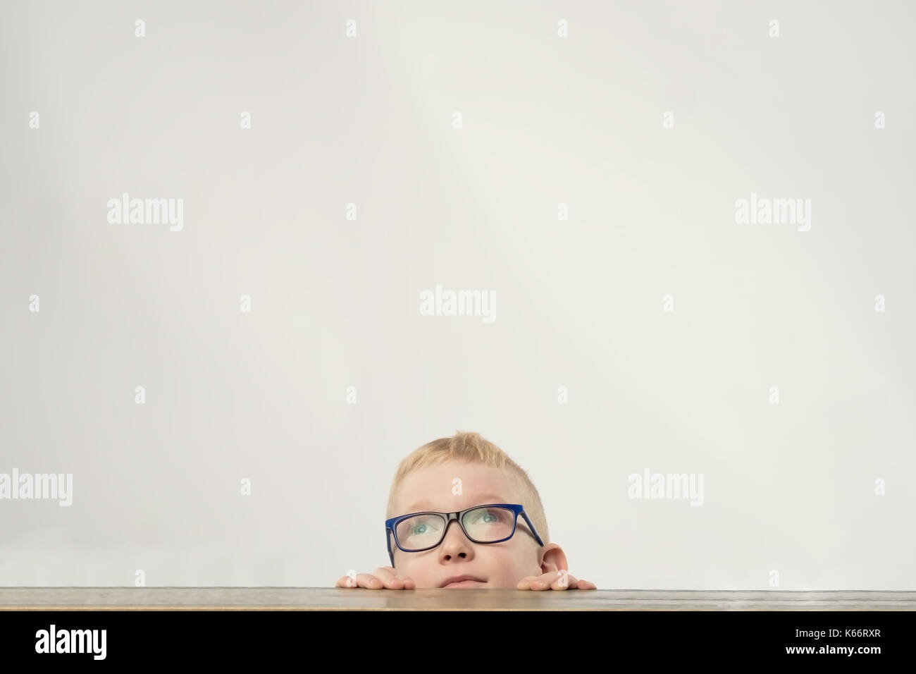 Lovely Young boy dans les verres se cacher et looking up Banque D'Images