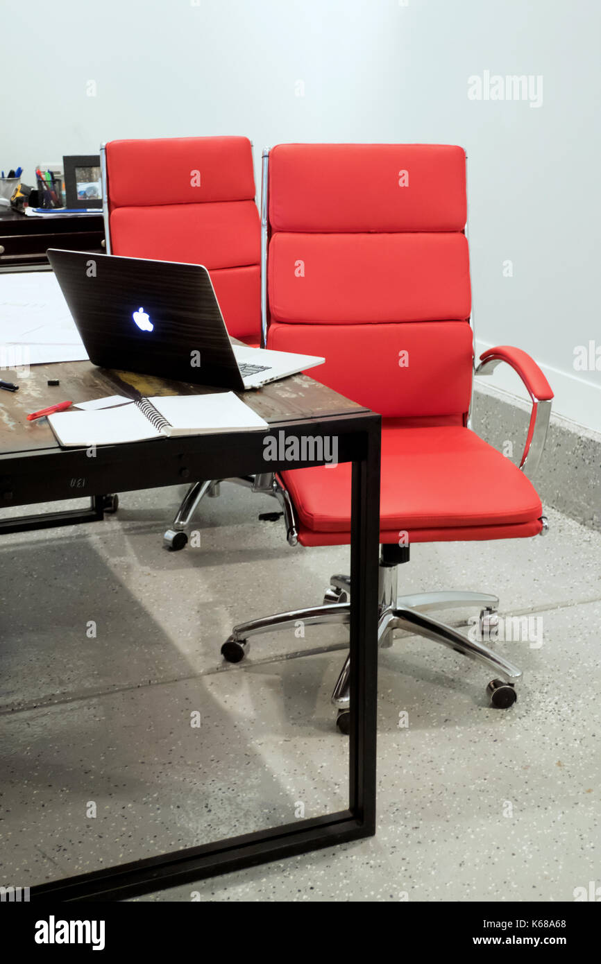 Deux chaises de bureau rouge assis à une table avec un livre de mac laptop sitting Ouvrir à côté d'une pile de papiers. Banque D'Images