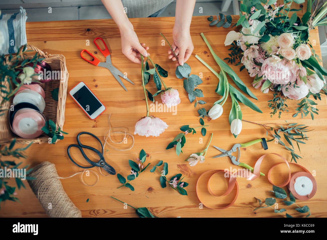 Mains d'un fleuriste contre desktop avec des outils de travail et rubans sur fond de bois Banque D'Images