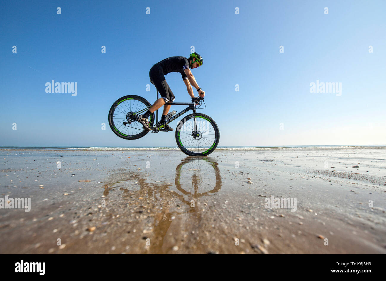 Pierre le Coq effectue un arrêt sur son vélo sur une plage vide à marée basse à Plérin, Bretagne. Banque D'Images