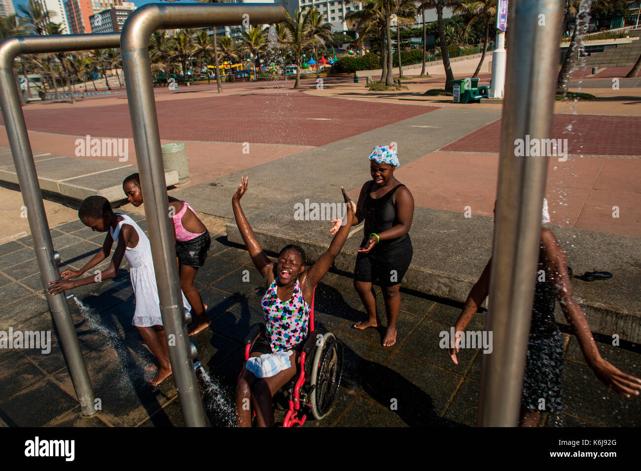 Les filles, dont un en fauteuil roulant, rire, jouer et une douche après avoir été dans les piscines publiques sur la promenade sur le Golden Mile de Durban, Afrique du Sud Banque D'Images