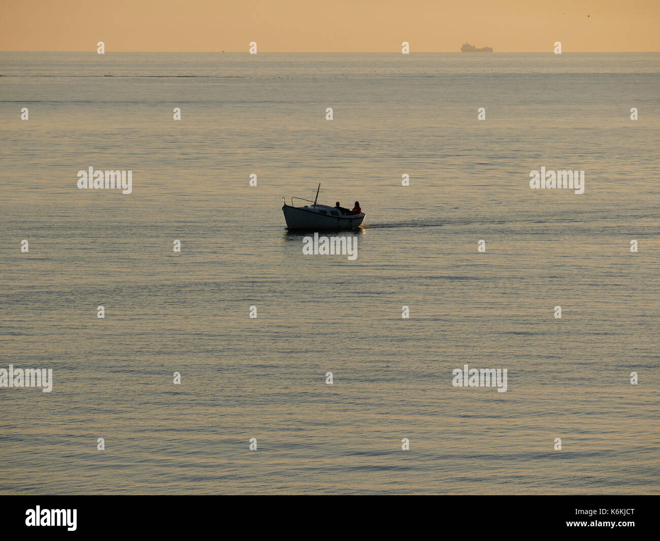Coucher de soleil à Hönö, Klåva dans l'archipel de Göteborg. Bateau avec deux personnes en passant, navire de fret en arrière-plan. Banque D'Images