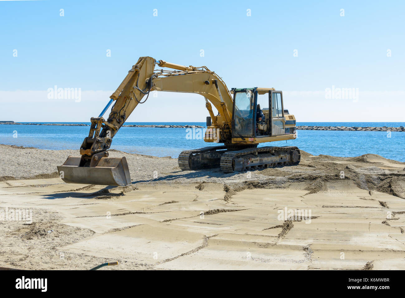 Que l'excavateur travaille sur la plage pour lisser le sable avant le début de la saison d'été Banque D'Images