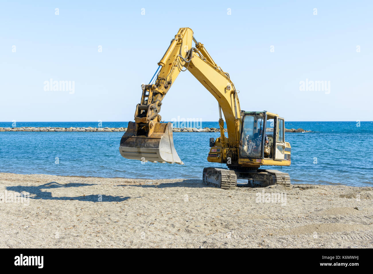 Que l'excavateur travaille sur la plage pour lisser le sable avant le début de la saison d'été Banque D'Images