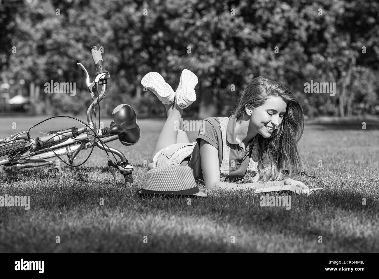 Shot monochrome d'une belle jeune femme se détendre au parc couché dans l'herbe lire un livre après l'actionnement de la nature en plein air loisirs bonheur e Banque D'Images