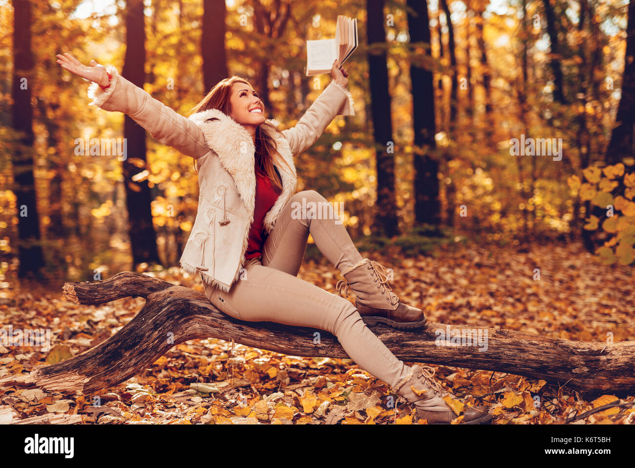 Belle jeune femme souriante holding book et s'amuser sous le soleil de forêt en automne les couleurs. Banque D'Images